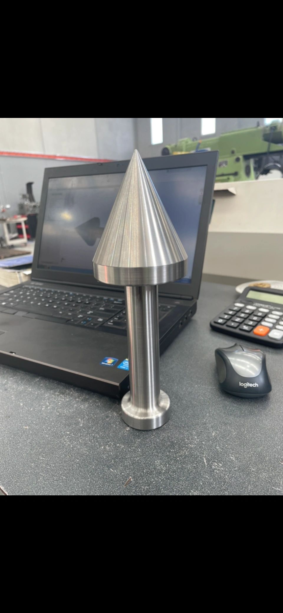 Steel conical centre point on workbench with CAD software in background